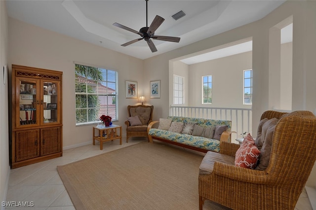 tiled living room with ceiling fan, a tray ceiling, and a healthy amount of sunlight