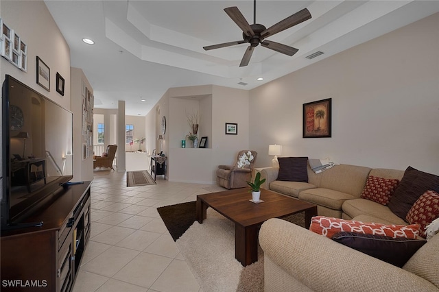 living room with ceiling fan, a tray ceiling, and light tile patterned floors