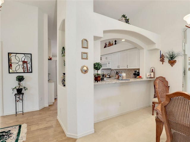 bar featuring white cabinetry, light hardwood / wood-style flooring, backsplash, a towering ceiling, and white appliances