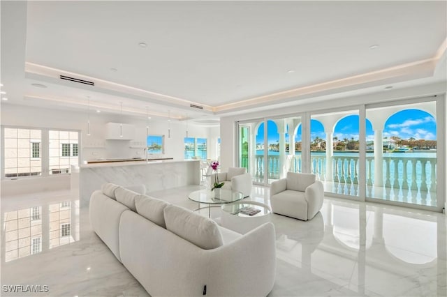 living room with a raised ceiling, sink, and a water view