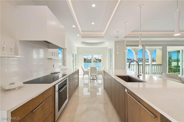 kitchen featuring stainless steel oven, a raised ceiling, sink, black electric cooktop, and decorative light fixtures