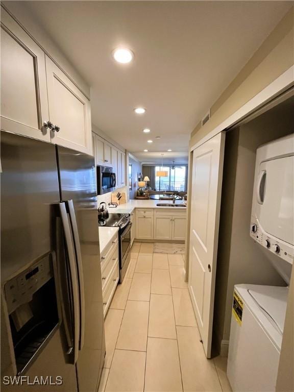 kitchen featuring white cabinets, stainless steel appliances, kitchen peninsula, stacked washing maching and dryer, and light tile patterned floors