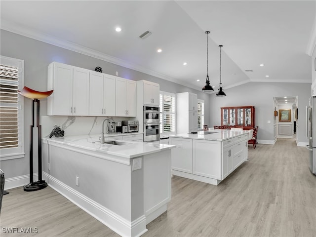 kitchen with decorative light fixtures, vaulted ceiling, kitchen peninsula, sink, and stainless steel appliances