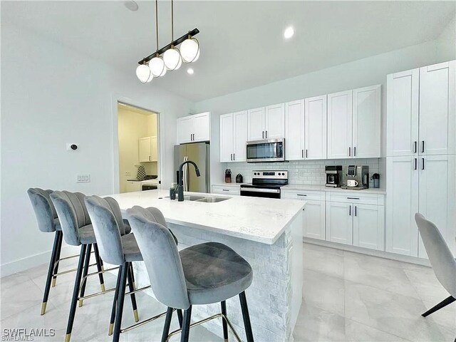 kitchen with pendant lighting, a kitchen island with sink, white cabinets, a kitchen breakfast bar, and stainless steel appliances