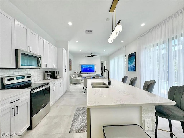 kitchen with pendant lighting, a kitchen breakfast bar, sink, ceiling fan, and appliances with stainless steel finishes