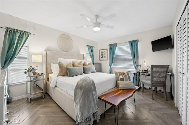 bedroom with multiple windows, ceiling fan, a closet, and parquet floors