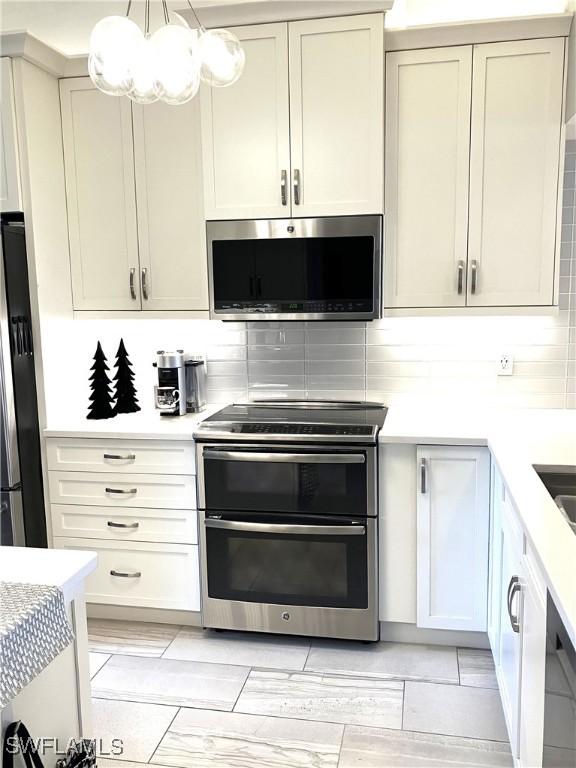 kitchen featuring decorative light fixtures, cream cabinets, tasteful backsplash, a notable chandelier, and appliances with stainless steel finishes