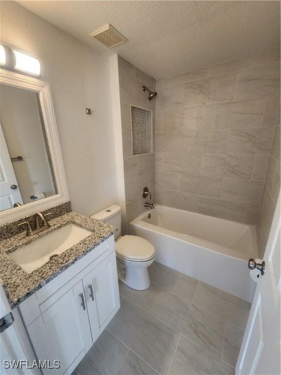 full bathroom featuring a textured ceiling, vanity, tiled shower / bath combo, and toilet