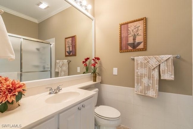 bathroom featuring vanity, a shower with door, toilet, ornamental molding, and tile walls