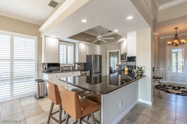 kitchen with white cabinetry, stainless steel appliances, pendant lighting, a breakfast bar, and ornamental molding