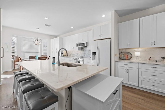 kitchen with white refrigerator with ice dispenser, decorative backsplash, white cabinetry, and an island with sink