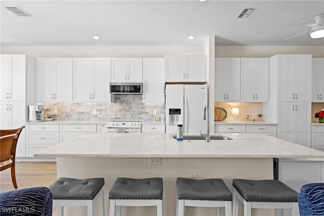 kitchen featuring light stone countertops, white appliances, white cabinetry, and an island with sink