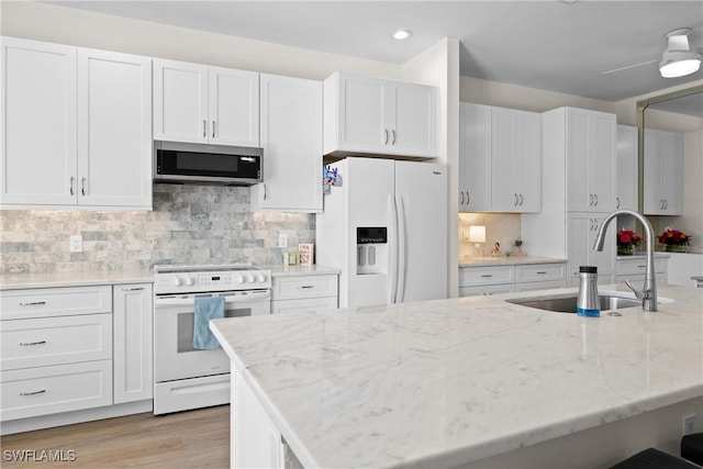 kitchen featuring sink, tasteful backsplash, light stone counters, white appliances, and white cabinets