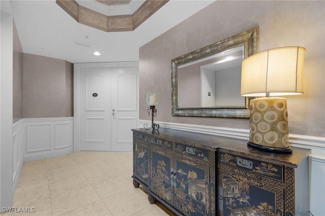 corridor featuring a tray ceiling, light tile patterned flooring, and ornamental molding