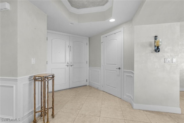 hall with light tile patterned floors, a tray ceiling, and ornamental molding