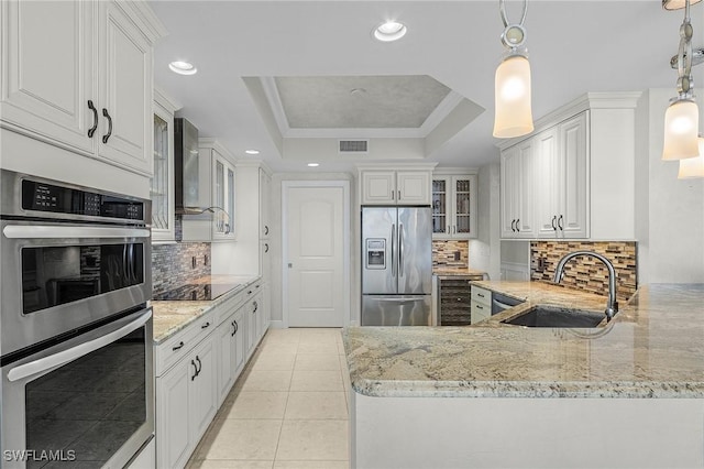 kitchen with sink, hanging light fixtures, a tray ceiling, white cabinetry, and stainless steel appliances