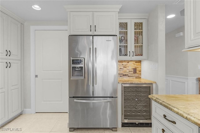 kitchen with light stone countertops, stainless steel refrigerator with ice dispenser, beverage cooler, light tile patterned floors, and white cabinets