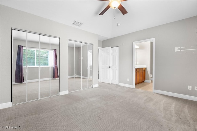 unfurnished bedroom with light colored carpet, ensuite bath, ceiling fan, and multiple closets