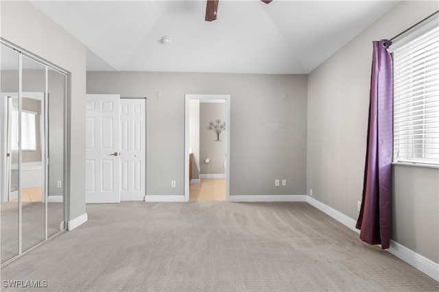 unfurnished bedroom with light carpet, ensuite bath, ceiling fan, multiple windows, and lofted ceiling