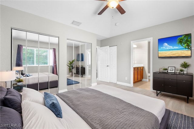 bedroom featuring ensuite bath, ceiling fan, light hardwood / wood-style flooring, and two closets