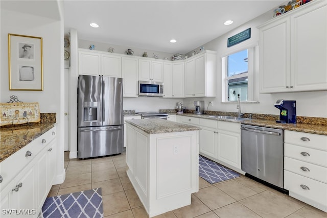 kitchen with sink, stainless steel appliances, a kitchen island, dark stone counters, and white cabinets