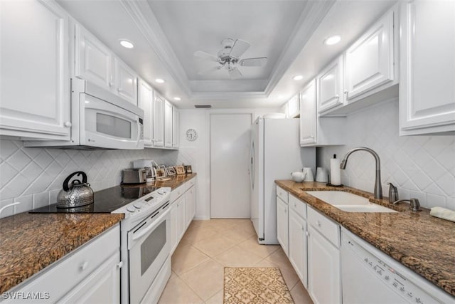 kitchen featuring a tray ceiling, white cabinets, dark stone counters, and white appliances