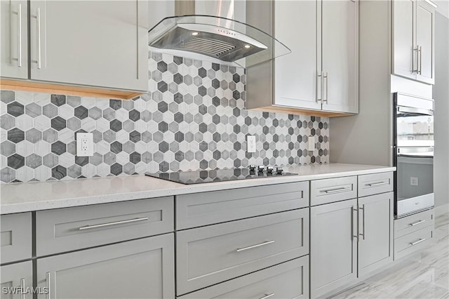 kitchen featuring light stone counters, backsplash, island exhaust hood, gray cabinets, and black electric cooktop