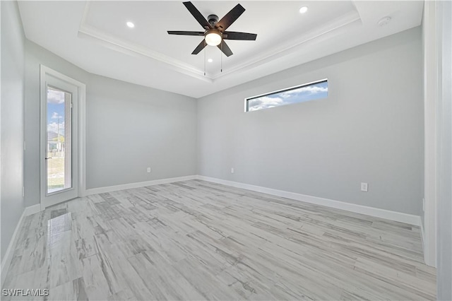 unfurnished room with ceiling fan, a healthy amount of sunlight, light wood-type flooring, and a tray ceiling