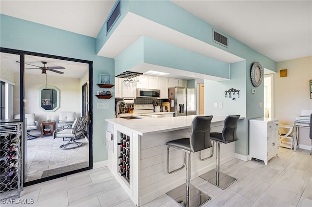 kitchen featuring stainless steel appliances, visible vents, a sink, a peninsula, and a kitchen bar