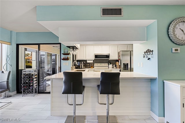 kitchen featuring kitchen peninsula, a breakfast bar, stainless steel appliances, and white cabinets