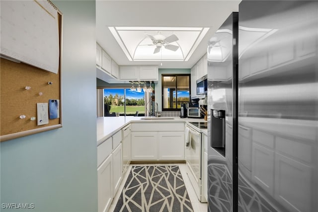 kitchen featuring appliances with stainless steel finishes, a raised ceiling, white cabinetry, and a sink