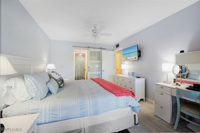 bedroom featuring ceiling fan, a barn door, visible vents, and light wood-style floors