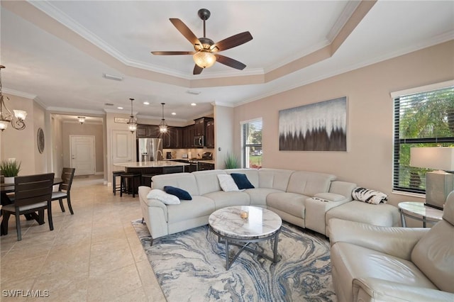 tiled living room with ceiling fan with notable chandelier, a raised ceiling, a healthy amount of sunlight, and crown molding