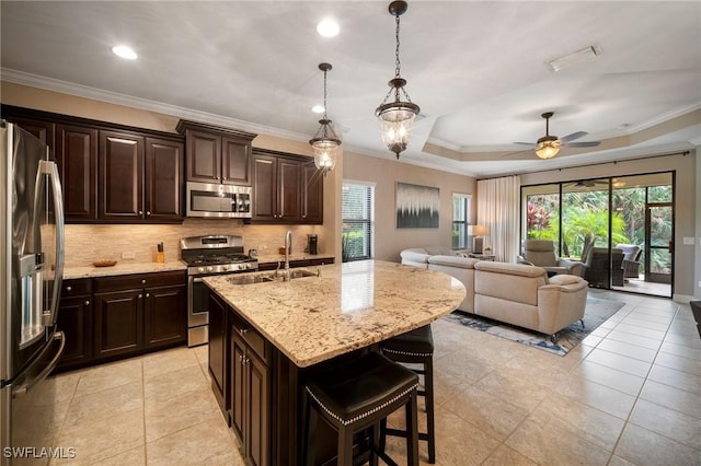 kitchen featuring sink, a raised ceiling, an island with sink, pendant lighting, and appliances with stainless steel finishes