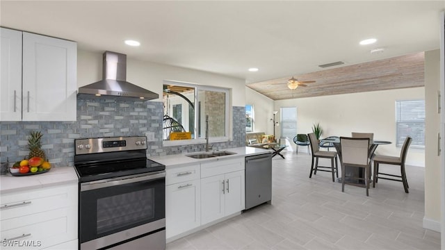 kitchen featuring decorative backsplash, white cabinetry, wall chimney range hood, and appliances with stainless steel finishes