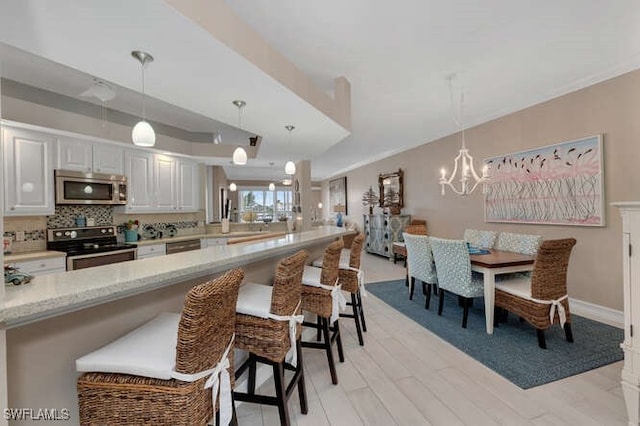 kitchen with light stone counters, white cabinetry, hanging light fixtures, and appliances with stainless steel finishes