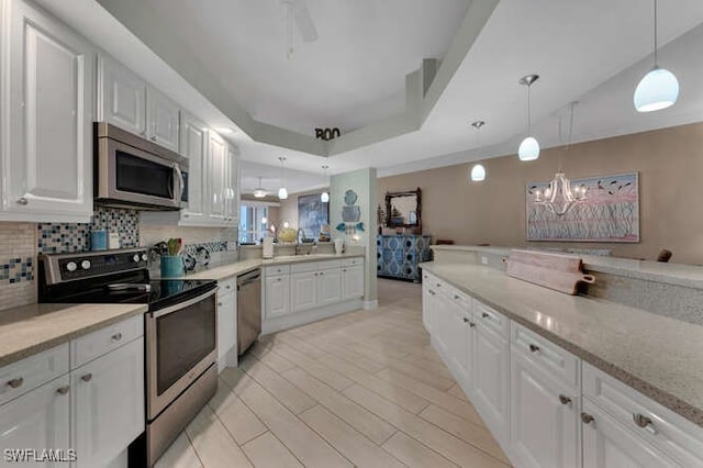 kitchen featuring a tray ceiling, decorative light fixtures, stainless steel appliances, and white cabinets