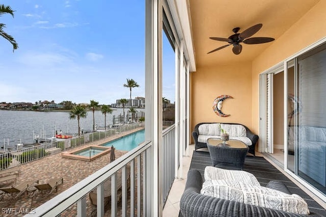 balcony with an in ground hot tub, a water view, and ceiling fan