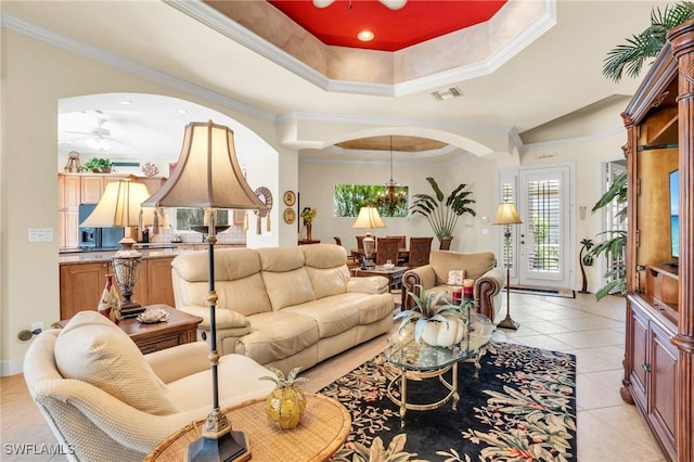 tiled living room featuring ceiling fan with notable chandelier, a raised ceiling, and ornamental molding