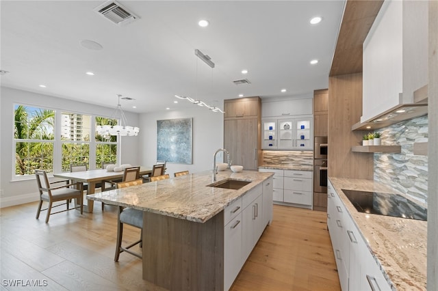 kitchen with white cabinets, decorative light fixtures, backsplash, a kitchen island with sink, and black electric cooktop