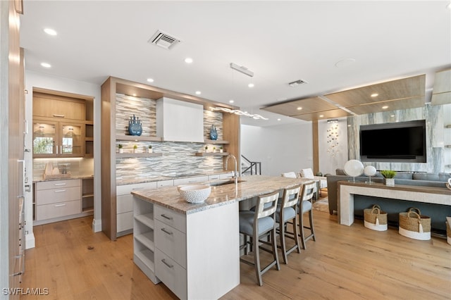 kitchen featuring a center island with sink, tasteful backsplash, light stone countertops, white cabinets, and sink