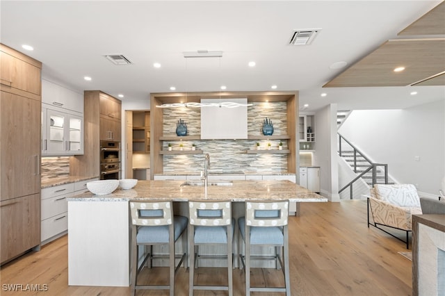 kitchen with a large island with sink, white cabinets, a kitchen bar, decorative backsplash, and light stone counters