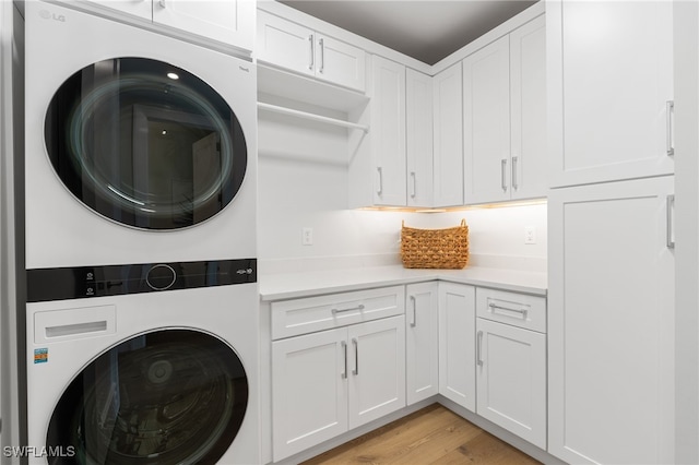 washroom featuring cabinets, stacked washer / drying machine, and light hardwood / wood-style flooring