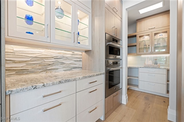 kitchen with light wood-type flooring, decorative backsplash, stainless steel double oven, and light stone countertops