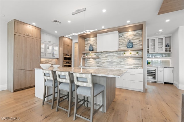 kitchen featuring a large island with sink, decorative backsplash, sink, white cabinets, and beverage cooler