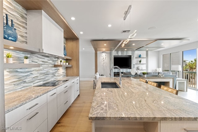 kitchen featuring black electric stovetop, white cabinets, a large island, and sink