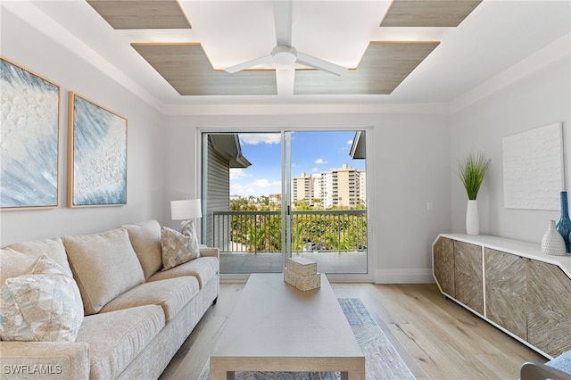 living room with ceiling fan, a tray ceiling, and light wood-type flooring