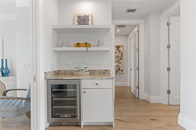 bar with light hardwood / wood-style floors and beverage cooler