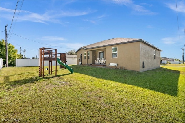 rear view of property featuring a playground and a lawn