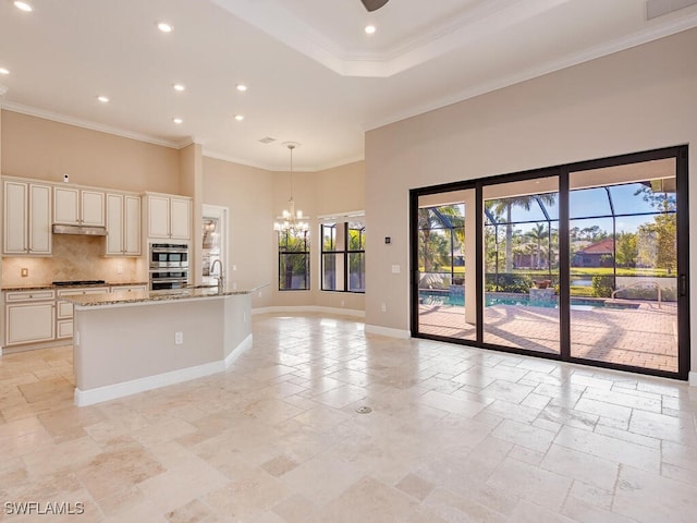 kitchen featuring light stone counters, pendant lighting, a center island with sink, gas cooktop, and crown molding